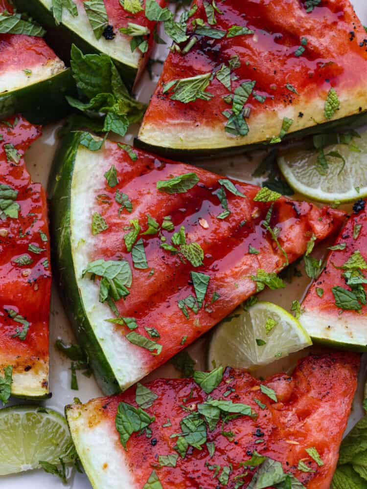 Grilling watermelon helps the sugars to caramelize and gives it a delicious hint of smoky flavor! Add a drizzle of honey lime sauce and fresh chopped mint on top for the ultimate refreshing side dish. Closeup of grilled watermelon, topped with freshly chopped mint.