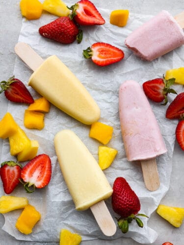 These fresh and fruity homemade popsicles will keep you cool all summer! They're naturally sweetened with honey and coconut milk for a refreshing, tasty treat. Multiple popsicles laid out on parchment paper.