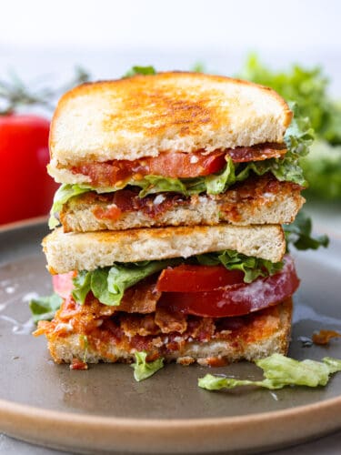 It's not hard to see why this classic summer sandwich is an American staple. BLTs are toasty, juicy, crispy, and flavorful - everything you could want from a sandwich! It's the perfect tasty lunch for a hot summer afternoon. A BLT sandwich cut in half and stacked on top of each other.