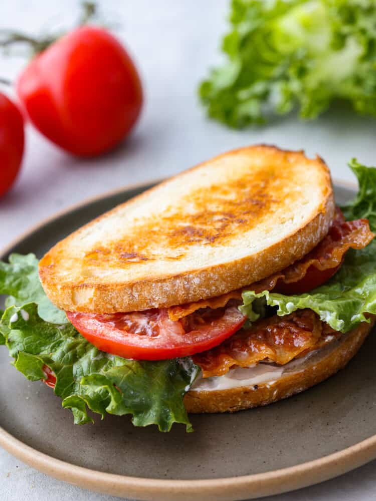 It's not hard to see why this classic summer sandwich is an American staple. BLTs are toasty, juicy, crispy, and flavorful - everything you could want from a sandwich! It's the perfect tasty lunch for a hot summer afternoon. Closeup of a sandwich topped with bacon, lettuce, and tomato on a gray plate.