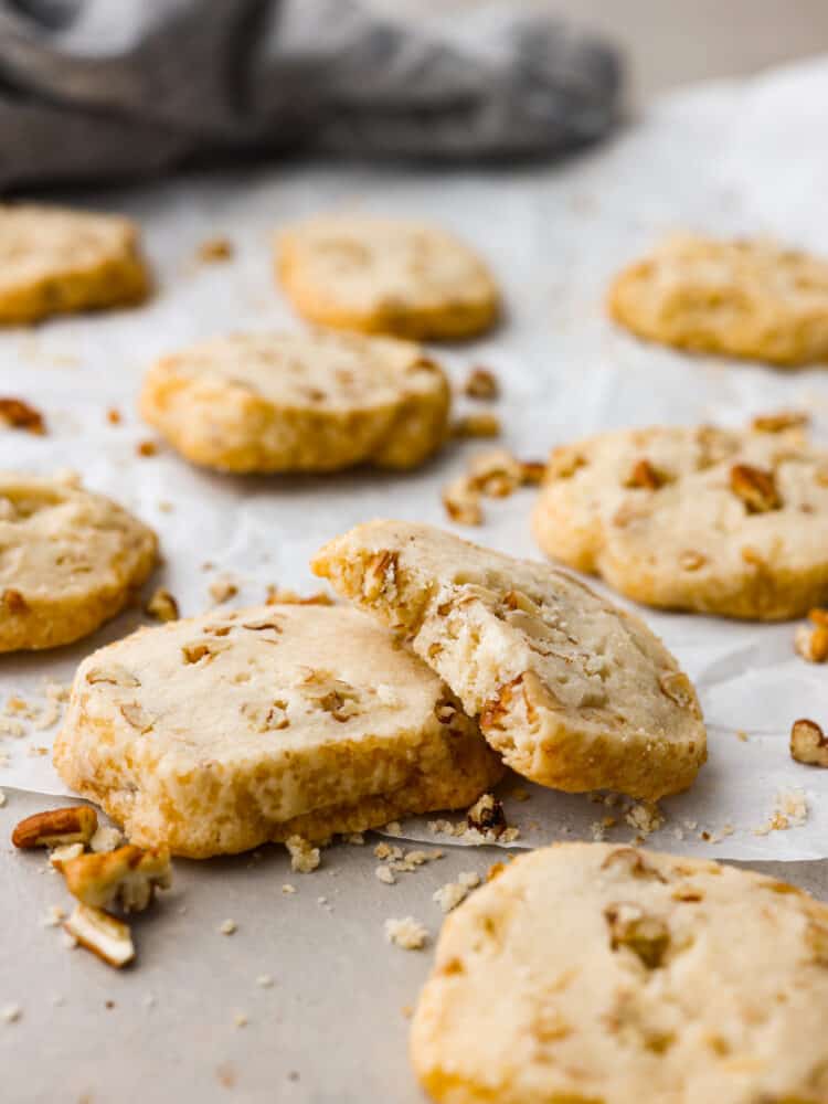 These pecan shortbread cookies are insanely delicious! They melt in your mouth with their fall-apart texture and sweet taste. The added texture of a crunchy pecan makes these practically perfect! Pecan shortbread cookies stacked on another. The top one is broken in half to show what the inside looks like.