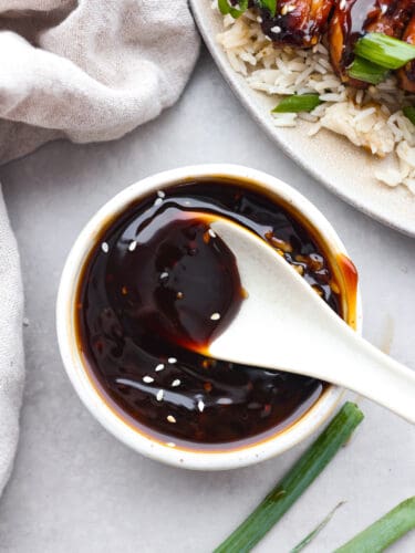 Yakitori sauce is a Japanese condiment traditionally used for grilled chicken skewers. Sweet, savory, and smoky, it's the perfect sauce to have on hand for all of your grilling needs this summer! Top-down view of yakitori sauce in a white bowl, being stirred with a spoon.