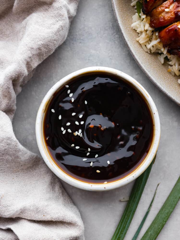Yakitori sauce is a Japanese condiment traditionally used for grilled chicken skewers. Sweet, savory, and smoky, it's the perfect sauce to have on hand for all of your grilling needs this summer! Yakitori sauce in a white bowl, garnished with sesame seeds.