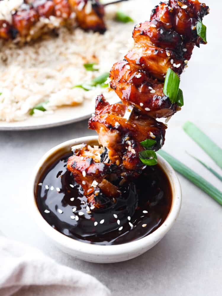 Yakitori sauce is a Japanese condiment traditionally used for grilled chicken skewers. Sweet, savory, and smoky, it's the perfect sauce to have on hand for all of your grilling needs this summer! Dipping a grilled chicken skewer into yakitori sauce.