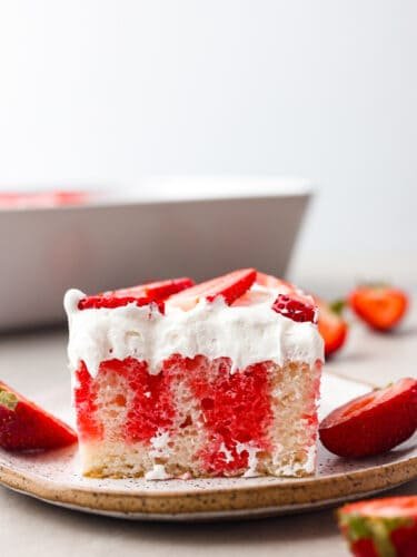 Incredibly light and tasty, this strawberry poke cake will be the star of any gathering! It's airy, soft, and brings that fresh strawberry taste into every single bite! The side view of a slice of poke cake on a plate.