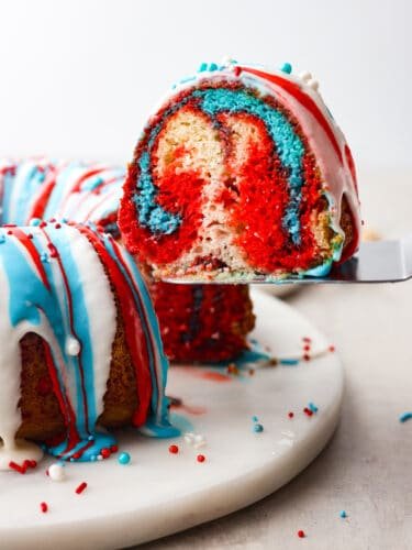 This firework bundt cake is exploding with colors and flavor! It not only looks impressive but it tastes so delicious that you will definitely be making this for every Fourth of July! The side view of a slice of firework bundt cake being served on a silver cake server.
