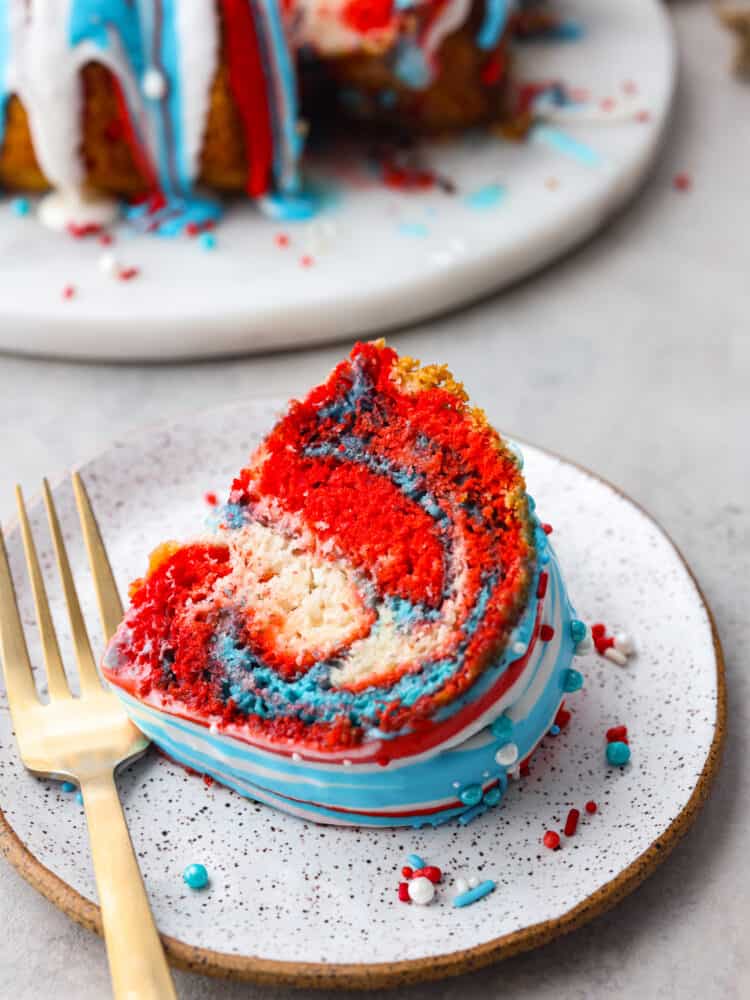 This firework bundt cake is exploding with colors and flavor! It not only looks impressive but it tastes so delicious that you will definitely be making this for every Fourth of July! A slice of firework bundt cake on a plate with a gold fork.