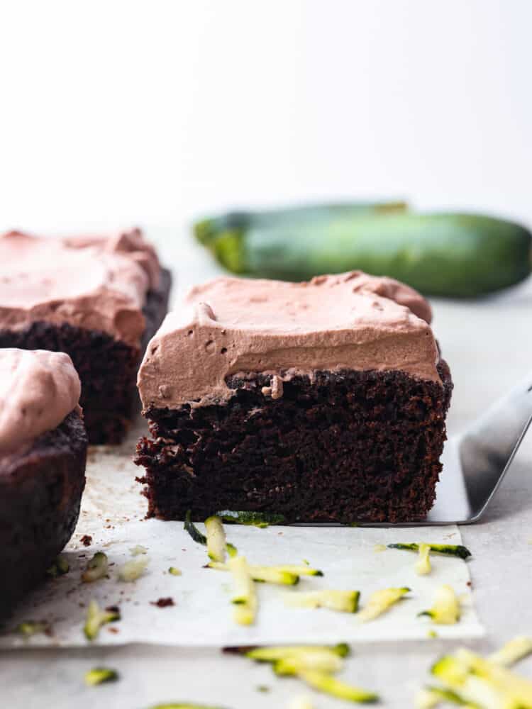 This Chocolate Zucchini Cake is a deep, dark chocolate cake that is topped with light and fluffy chocolate whipped cream! With 3 cups of zucchini, it is incredibly moist and you won't even notice all the vegetables! The side view of a slice of chocolate zucchini cake.