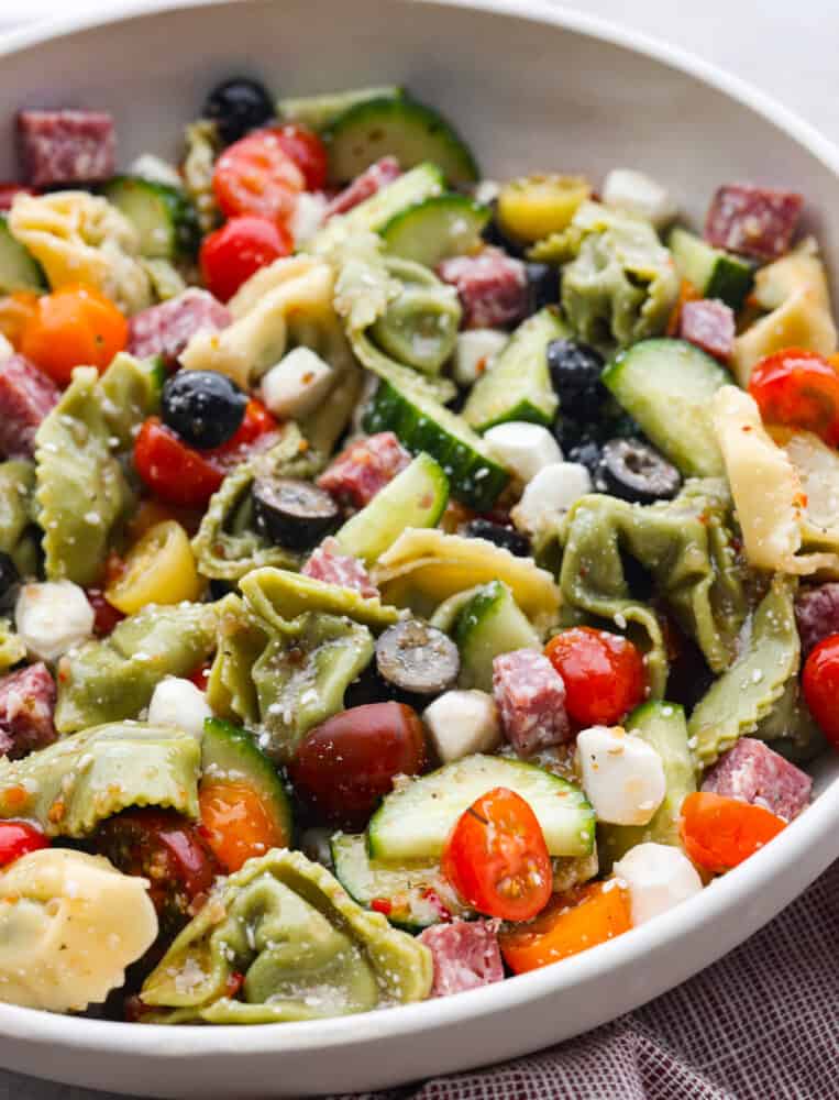 Easy Italian tortellini pasta salad is full of fresh summer veggies, salami, and tortellini pasta. It is tossed in a zesty Italian dressing and is always the hit of the potluck! A close up of a bowl of Italian Tortellini Pasta Salad.