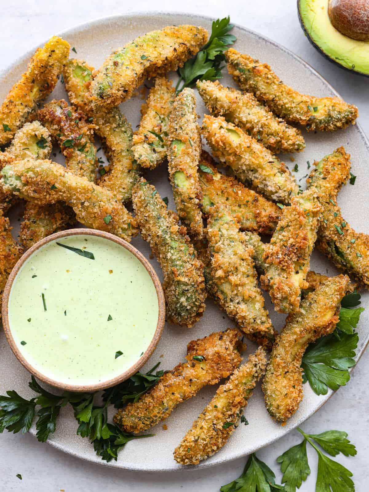 Insanely delicious and perfect for dipping, these fried avocado slices are the best appetizer choice! You're going to love their crispy, golden panko shell and buttery, creamy center. Top-down view of fried avocado slices on a gray plate served with dipping sauce.