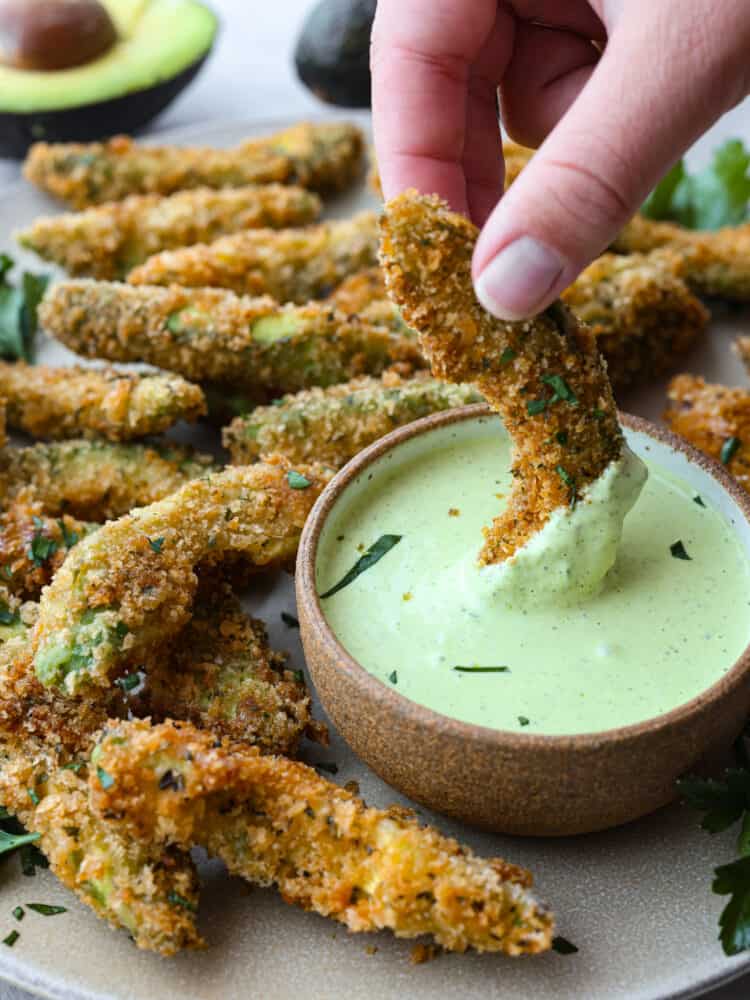 Insanely delicious and perfect for dipping, these fried avocado slices are the best appetizer choice! You're going to love their crispy, golden panko shell and buttery, creamy center. Closeup of an avocado fry being dipped in sauce.